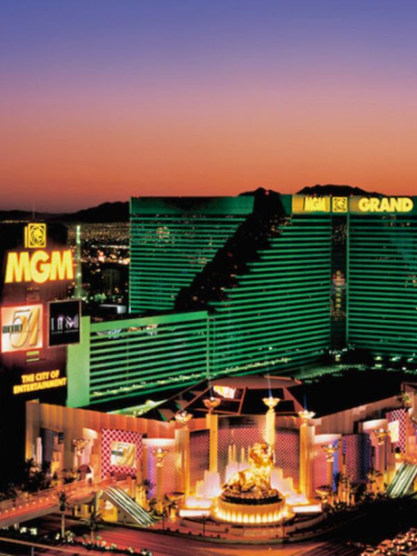 MGM Grand zeleně osvětlený hotel MGM Grand v Las Vegas, budova zářící večerním osvětlením, atmosféra za soumraku, světla hotelu se odrážejí na okolních plochách, ruch města v pozadí, moderní luxusní architektura