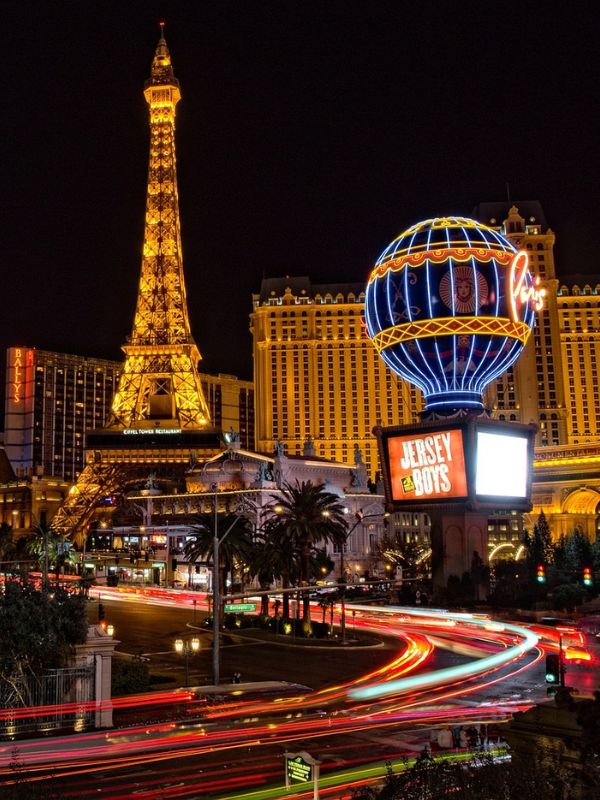 letecký pohled na osvětlené Las Vegas, zářící mrakodrapy, neonové nápisy, rušná hlavní ulice Strip v noci, barevné světelné efekty, okolní poušť viditelná v dálce