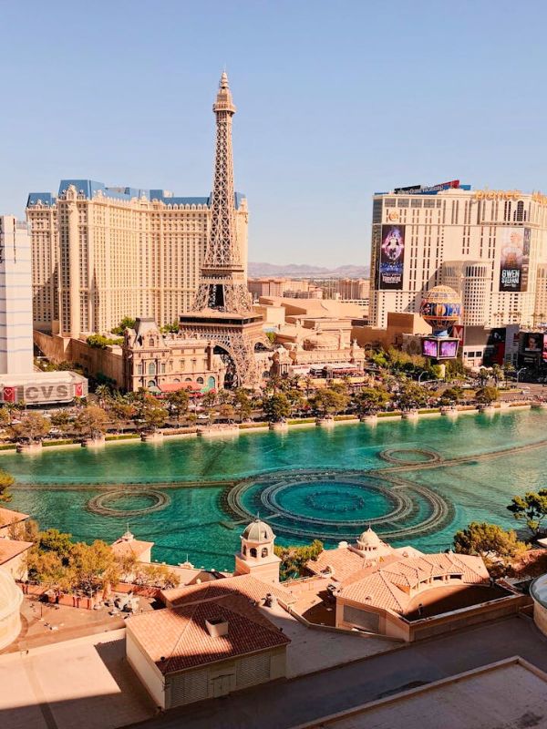 Paris pohled na město Las Vegas, vysoké hotely a kasina, Eiffelova věž v pozadí, fontána před ní vypnutá, denní nebo večerní světlo, moderní architektura, rušná městská scéna, jasná obloha