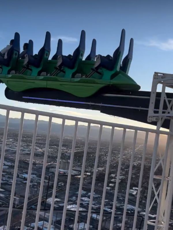 The Strat atrakce na vrcholu Stratosphere Tower v Las Vegas, zelený kolotoč vysokou nad městem, panoramatický pohled na Las Vegas v pozadí, slunečný den, vzrušující adrenalinová atmosféra, lidé na kolotoči, město a poušť viditelné daleko pod atrakcí