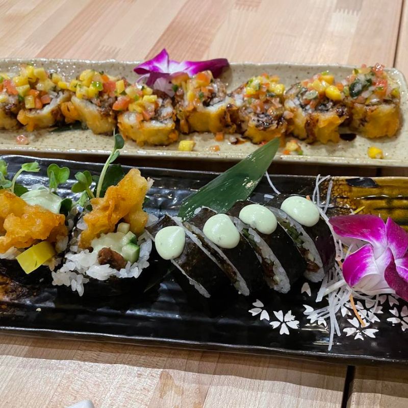 Vegan Sushi veganské sushi v Las Vegas, talíř barevného sushi s avokádem, okurkou, mrkví, řasou a rýží, ozdobené sezamovými semínky a pikantními omáčkami, moderní prezentace na stylovém talíři, svěží a zdravá atmosféra, restaurace v pozadí s jemným osvětlením