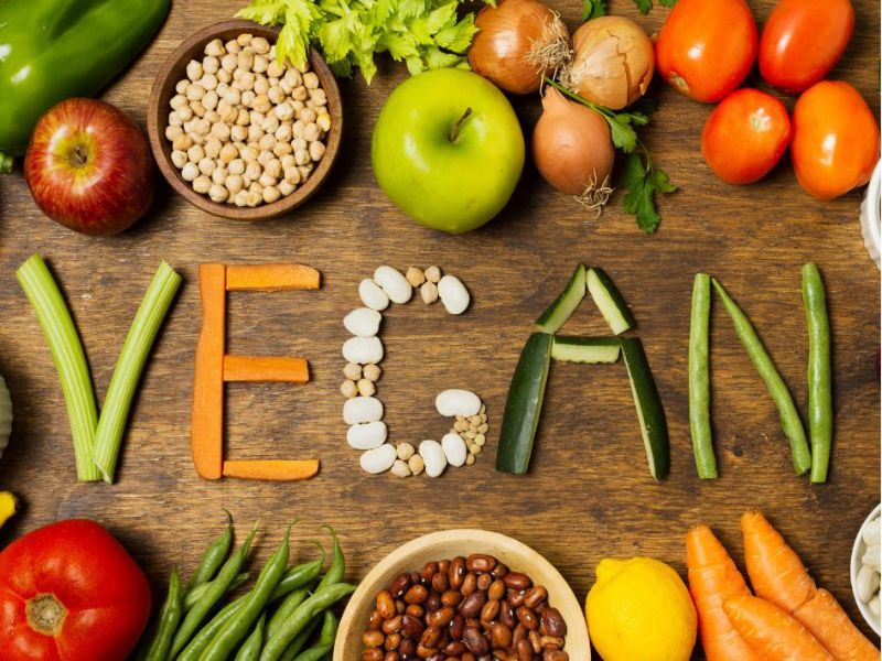 Ovoce a zelenina na dřevěném prkénku uprostřed z kousků zeleniny vytvořený nápis VEGAN