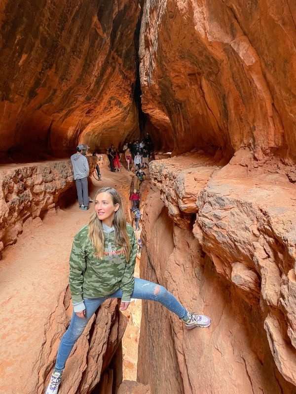 Žena stojí nad prasklinou ve skále na túře **Soldiers Pass** v Sedoně v Arizoně.