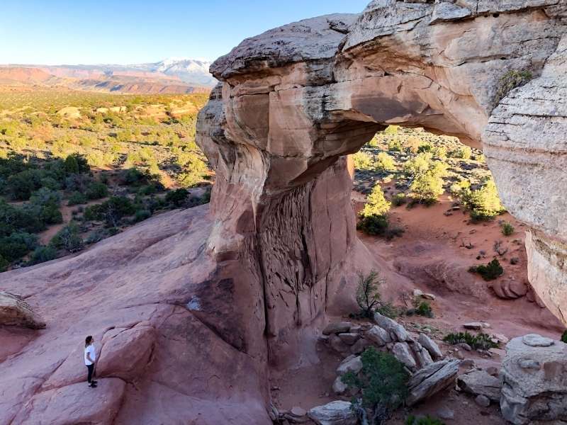 Skalní útvar ve tvaru velkého oblouku, vegetace a modrá obloha.