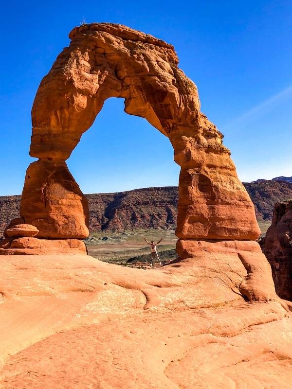 Muž pózuje u Delicate Arch v Utahu.