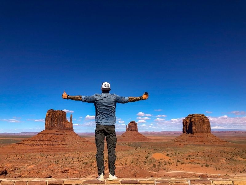 Muž roztahuje ruce před Monument Valley.
