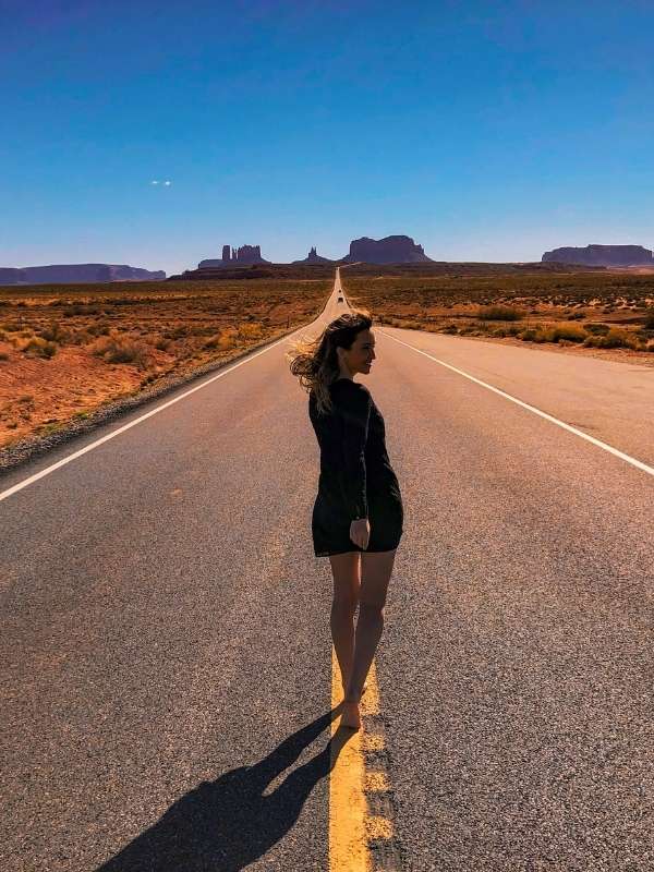 Žena pózuje na dlouhé silnici v Utahu, v pozadí Monument Valley.