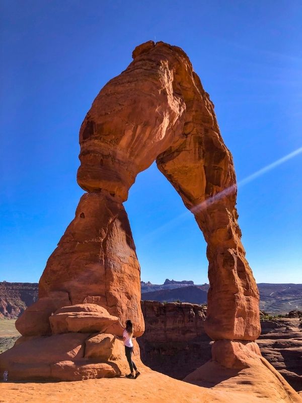 Žena stojí u Delicate Arch v Utahu, modrá obloha.