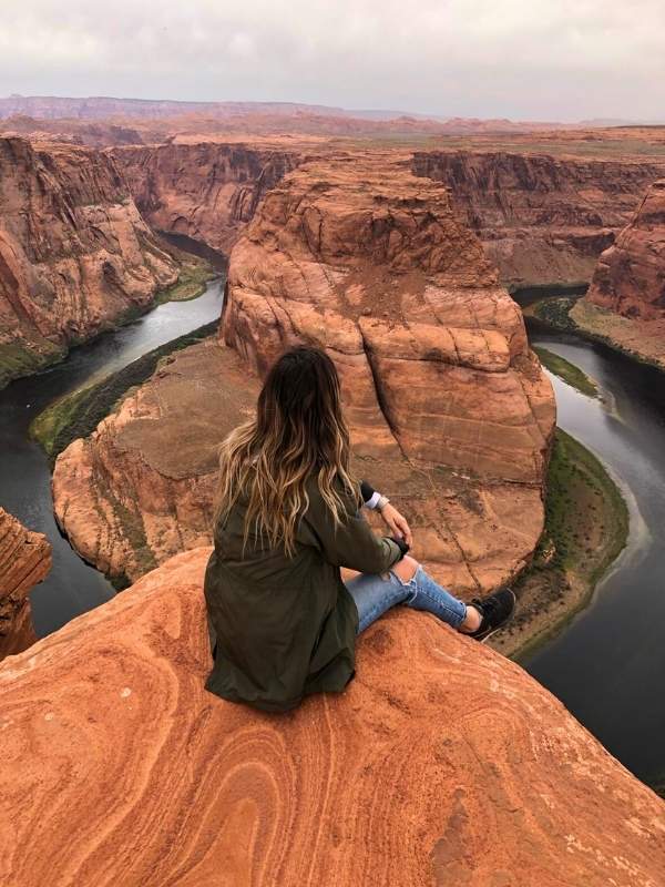 Žena sedící na okraji známého Horseshoe Bendu v Arizoně, pod ní se v hlubokém kaňonu klikatí řeka Colorado.
