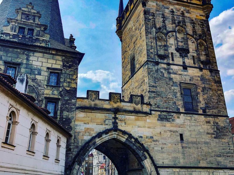 Historická kamenná věž s propracovanými detaily a klenutou bránou pod modrou oblohou; vyvolává pocit středověké architektury a nadčasovosti.