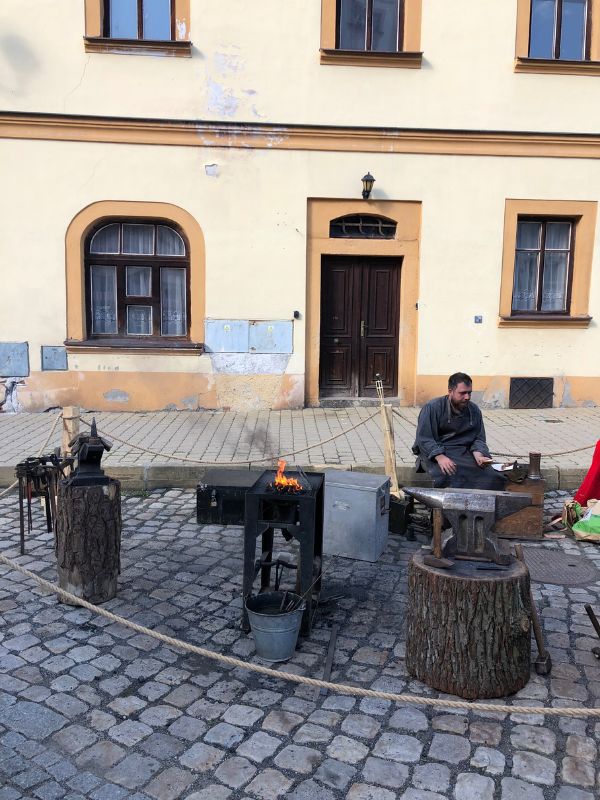 Kovář pracuje se železem před historickou budovou v Lokti.