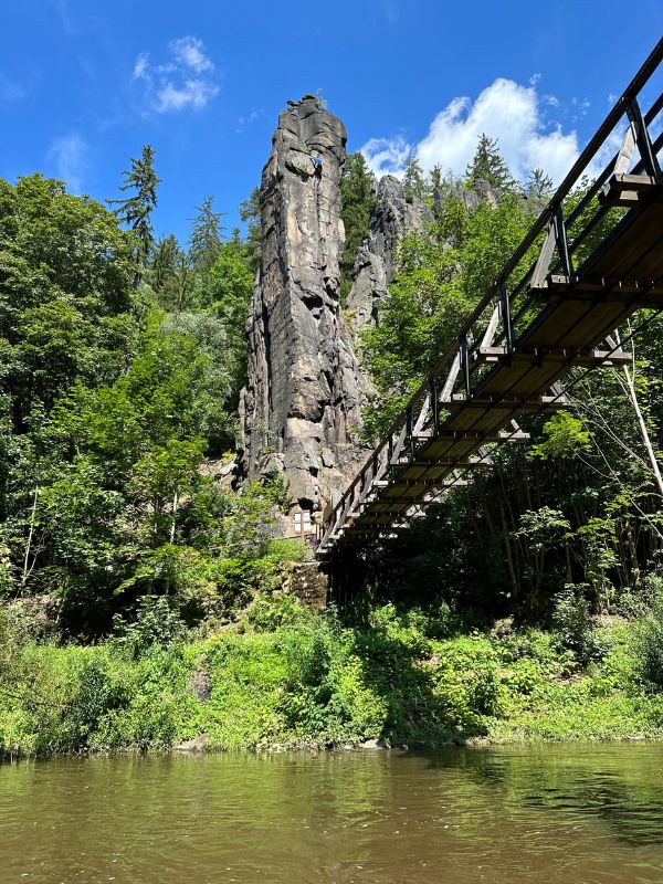 Most přes Svatošské skály, které se tyčí nad ním, obklopený zeleným lesem a pod modrou oblohou.
