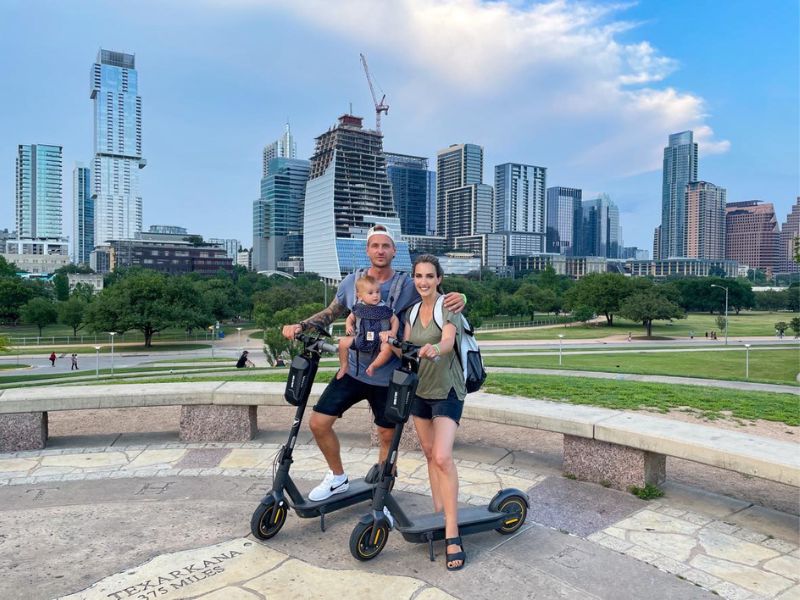 Rodina na elektrokoloběžkách, za nimi park a město Austin.