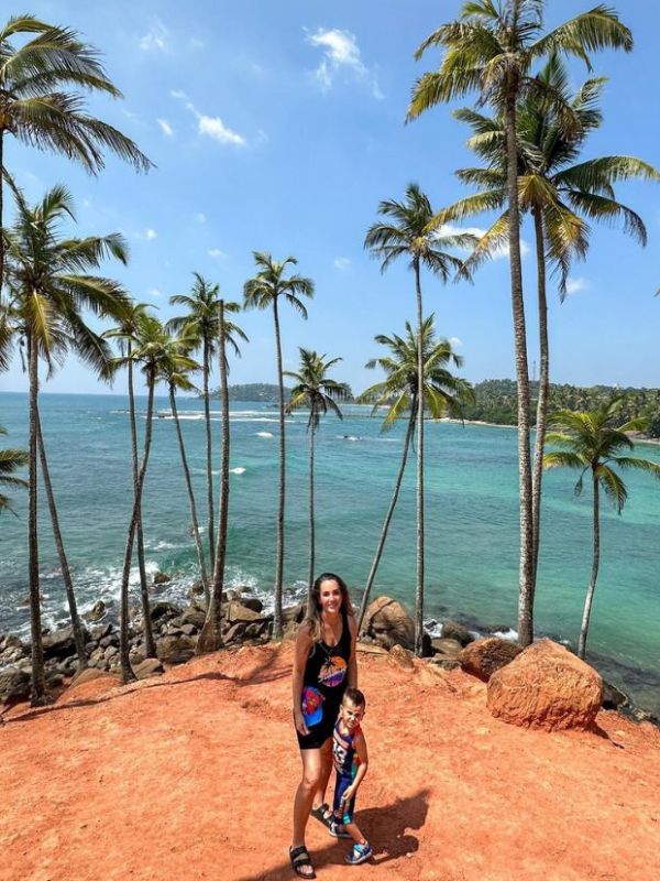 Coconut Hill žena s chlapcem stojí obklopeni vysokými palmami, za nimi oceán a modrá obloha na Coconut Hill na Srí Lance