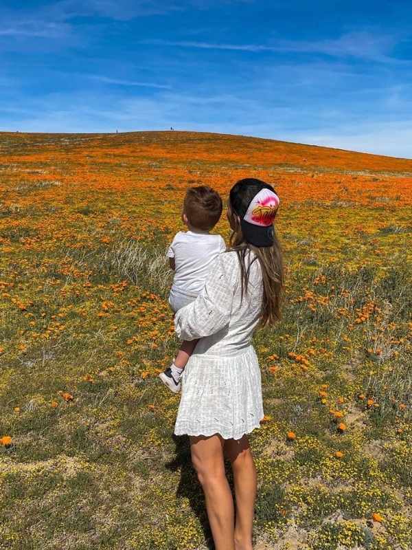 Matka v bílých šatech drží syna a oba koukají do pole vlčích máků