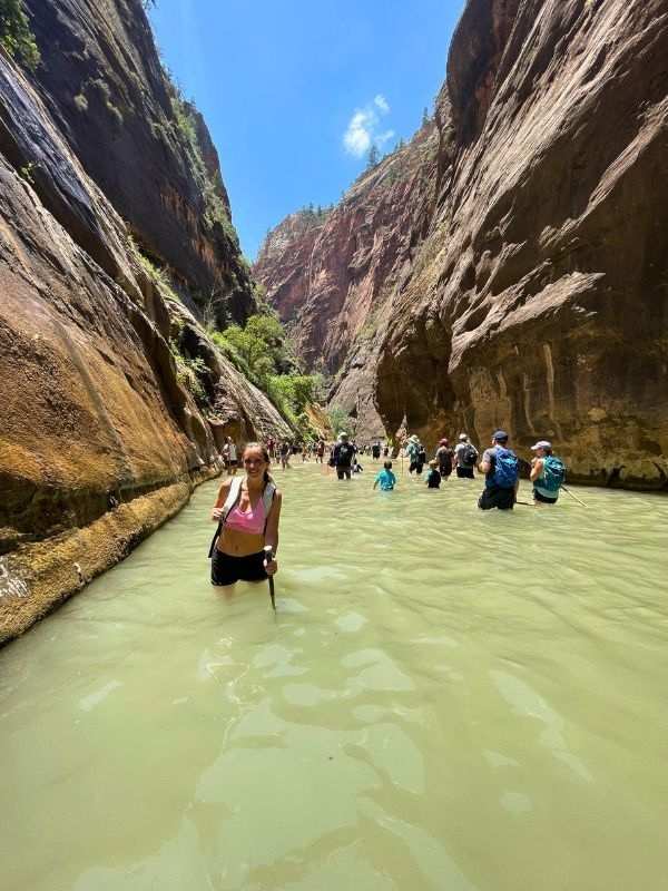 Hiking Zion NP žena stojí po pás ve vodě na stezce The Narrows v Utahu, kolem se tyčí vysoké skály