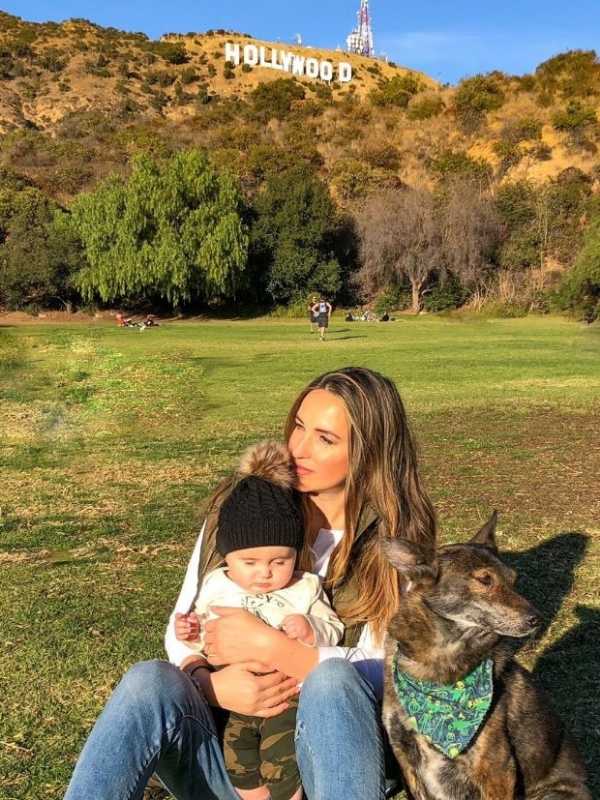 žena, syn a pes sedí na trávě pod kopcem s nápisem Hollywood