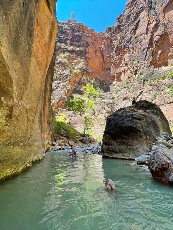 In Zion The Narrows v národním parku Zion, velký balvan s mužem stojícím na vrcholu, kolem proudící voda a vysoké skály