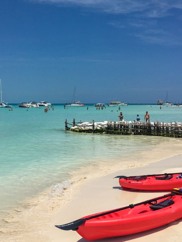 Isla Mujeres dva červené kajaky stojí na bílé pláži, tyrkysové moře, Isla Mujeres a molo v pozadí