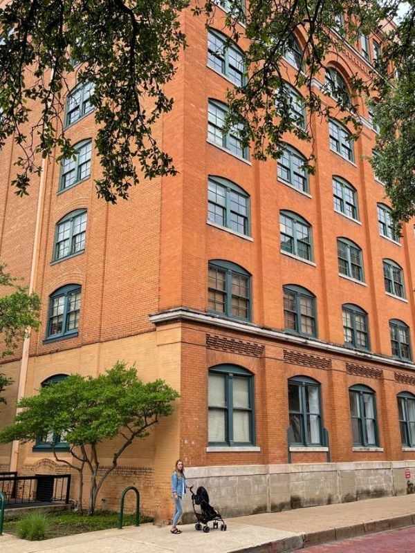 Žena s kočárkem stojí před vysokou cihlovou budovou, kde byl v Dallasu zastřelen bývalý prezident USA John F. Kennedy.