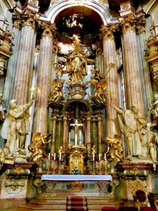 Honosná chrámová síň s vysokými stropy a sloupy, zdobená zlatými sochami a křížem