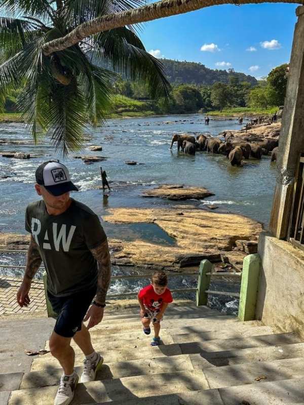 muž a dítě vycházejí po schodech, za nimi se koupající stádo slonů v řece