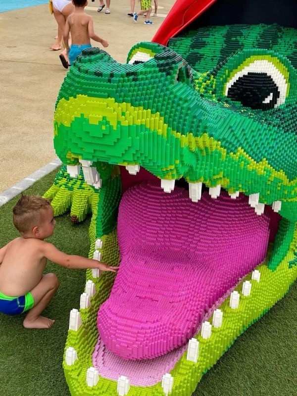 **Velká hlava krokodýla z Lega, malý chlapec natahuje ruku do obří tlamy.**