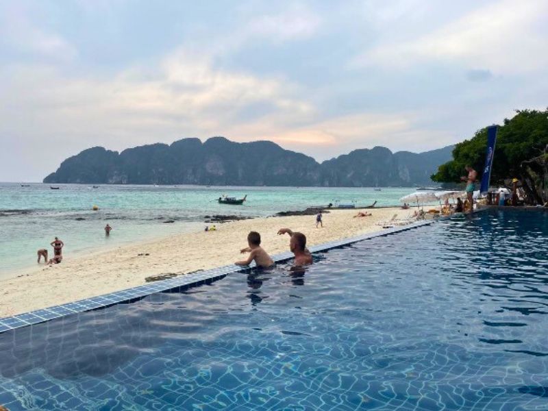 Dvě osoby se koupou v infinity bazénu, za nimi je pláž a oceán