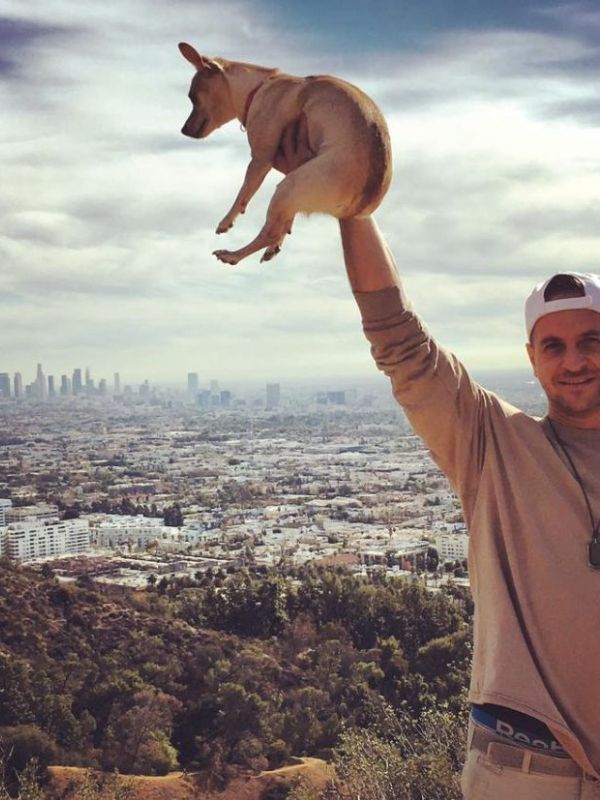 muž drží malého psa nad hlavou, v pozadí celé město Los Angeles