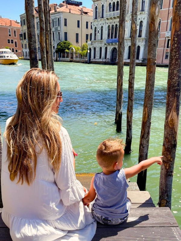 žena a syn sedí na molu u řeky v Benátkách