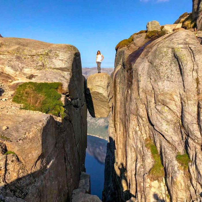 Žena stojí na zaklíněném kameni vysoko nad vodou v Norsku