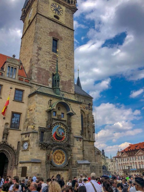 Věž s pražským orlojem, pod kterou stojí lidé, na pozadí modré oblohy