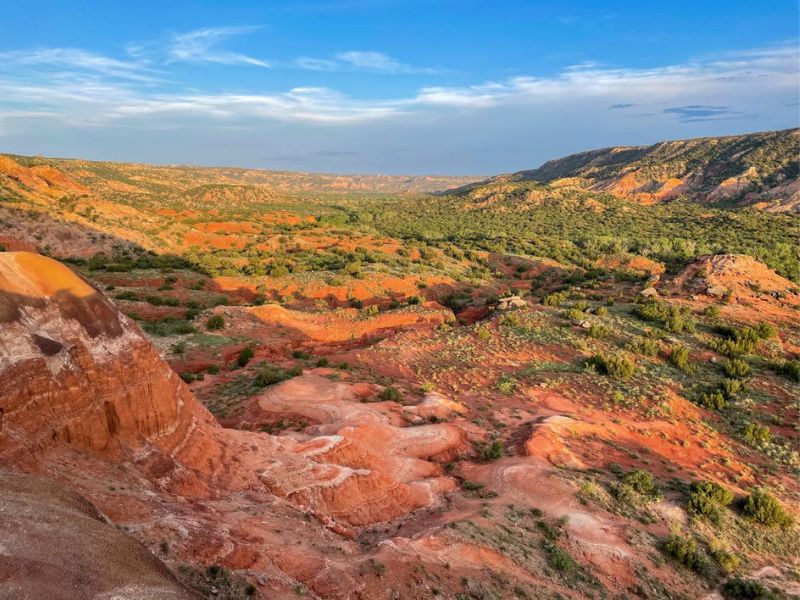 Palo Duro Park s červenou hlínou, modrou oblohou a zelenými ostrůvky.