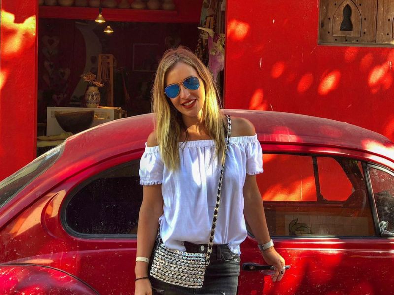 Žena stojí před červeným zaprášeným vozem VW.