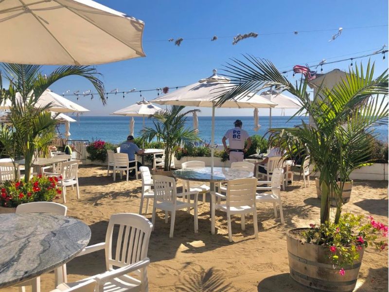 Paradise Cove restaurace v Malibu, bílé stoly a slunečníky v písku, v pozadí oceán