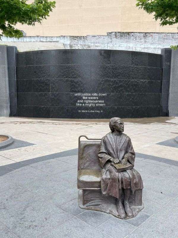 Socha Rosy Parks sedící na dvousedačce, vedle velkého památníku s citátem od M. L. Kinga Jr.