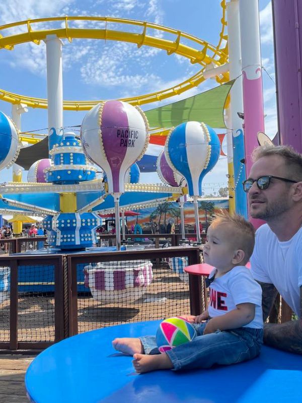 Santa Monica Pier se žlutou dráhou, barevnými balonky a mužem držícím své dítě