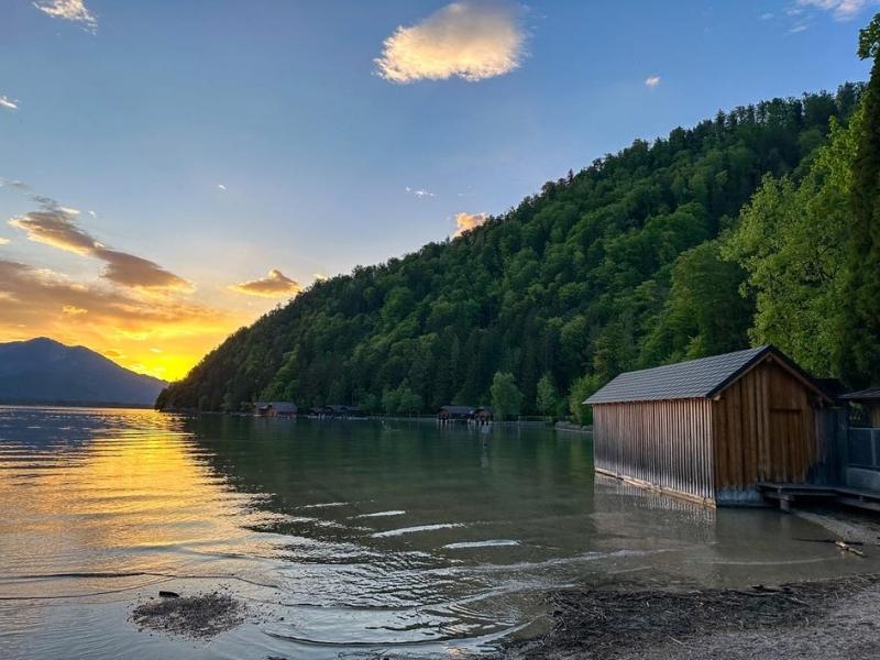 Západ slunce nad vodou, zelené hory a dřevěná bouda
