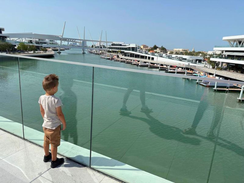 UAE Abu Dhabi Marina v Abú Dhabí, malý chlapec sleduje vodu a odraz okolních budov na hladině