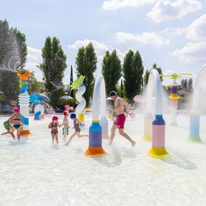 **Děti i dospělí pobíhají mezi stříkající vodou v bazénku.**