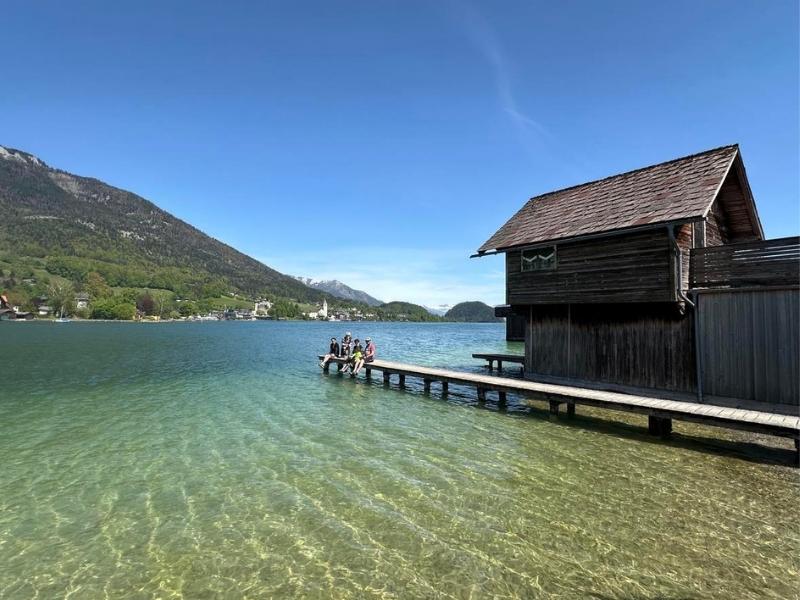 Dřevěná bouda s molem u průzračné vody a horami v pozadí