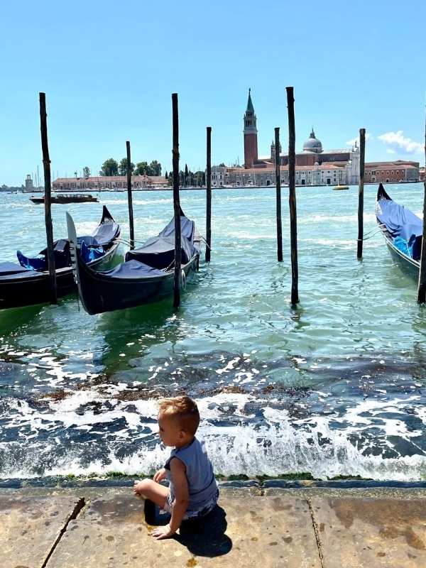 malý chlapec obklopený loďmi, v dáli jsou Benátky