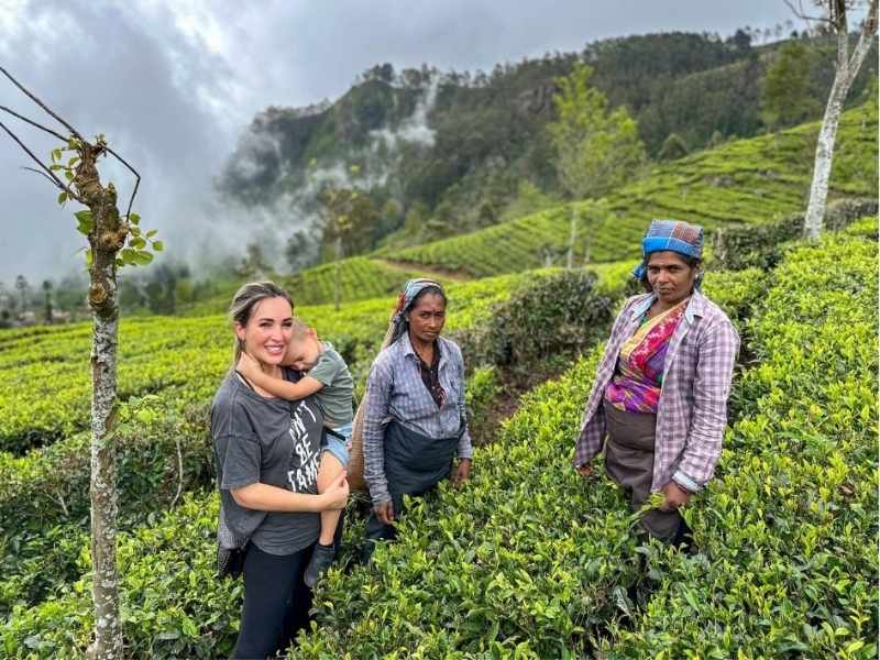 tři ženy stojí v čajových plantážích, jedna drží malé dítě