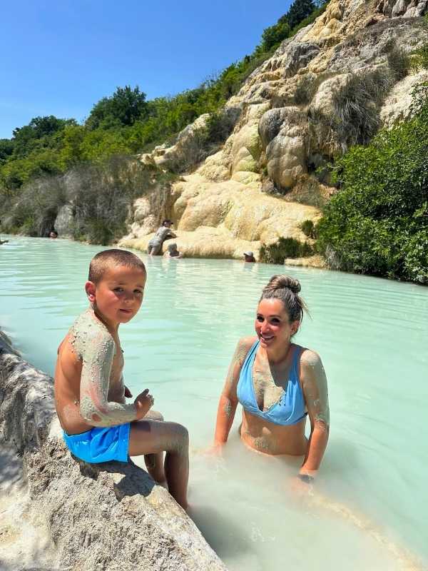 Žena a syn v modrých plavkách ponoření do světle modré vody termálních pramenů v Bagno Vignoni.