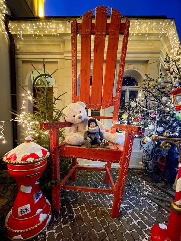 Chlapec sedí na velké červené židli ve vánočním domě v Karlových Varech, kolem vánoční ozdoby.