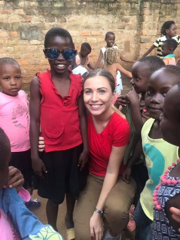 Bílá dívka v červeném tričku objímá černošského chlapce v červeném tričku, kolem se hraje skupinka dětí