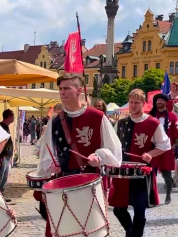 Muž v zimním kabátě a klobouku hraje na flétnu v Lokti.