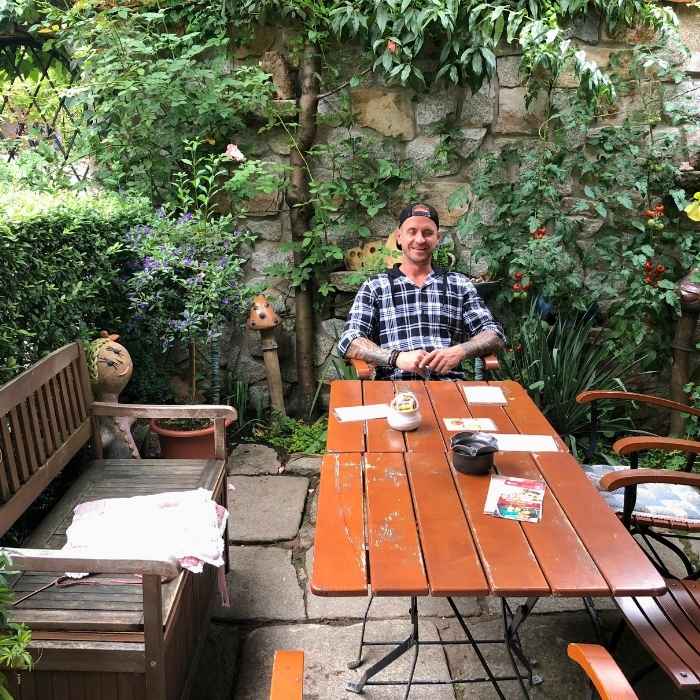 Muž sedí u stolu obklopen zelení v Lokti.