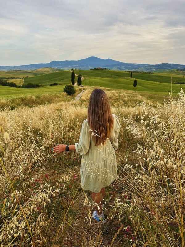 Žena hladí klasy pole, lemovaného cestou a kopci v Pienze v Itálii.