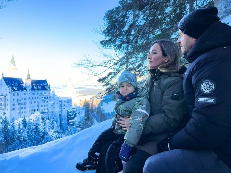 Rodina s malým chlapcem pózuje před zasněženým zámkem Neuschwanstein.